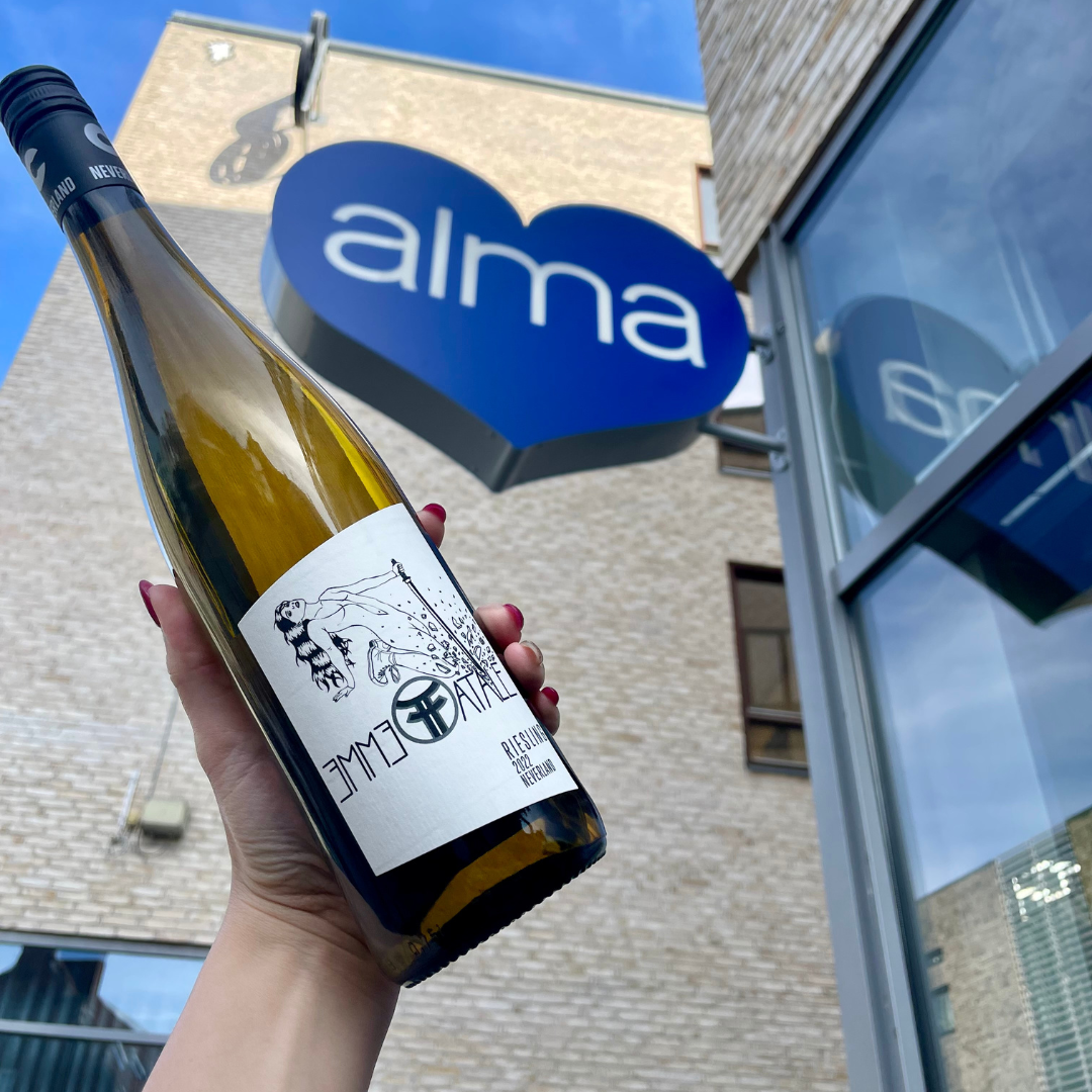 A bottle of Femme Fatale riesling by Neverland Vineyards raised next to Alma food market's store sign in Copenhagen
